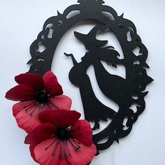 two red flowers are sitting in front of a black metal wall decoration with a silhouette of a woman