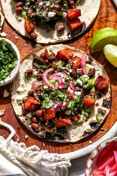 two tortillas with meat and vegetables on a wooden cutting board next to sliced limes