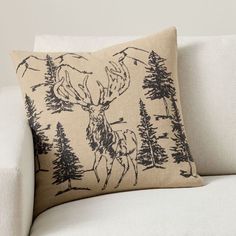 a white couch with a deer pillow on it's back and trees in the background