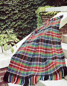 a colorful blanket sitting on top of a stone step next to a brick wall and shrubbery