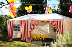 a large tent with red and white striped curtains, yellow chairs and balloons hanging from the ceiling