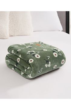 a green blanket with white flowers on it sitting on top of a neatly made bed