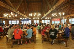 several people sitting at tables in a large room with wooden floors and beams on the ceiling