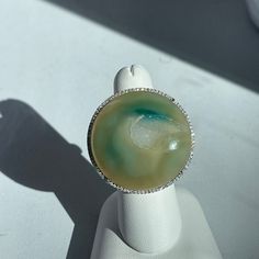 Very large, statement ring in 18KT white gold, with round multi-tone agate geode druzy ring. Stunning blue/ green agate geode with open mineral crystal deposits. Size 7.5 Can be resized for an additional fee Weight: 19 grams Stone measures: 40mm Stamped 18K Micropave Diamonds Halo .75 CT diamond; SI Clarity; H Color Fine Jewelry Agate Gemstone, Luxury Round Agate Rings, Luxury Round Agate Jewelry With Large Stone, Luxury Agate Ring Jewelry, Luxury Round Chalcedony Jewelry, Silver Agate Geode With Natural Stones, Unique Round Gemstone Geodes, Unique Silver Geode With Gemstone Details, Luxury Agate Cabochon Rings