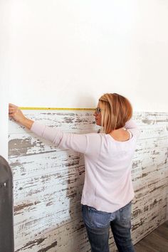 a woman measuring the width of a wall with a tape measure on it's side