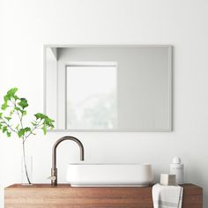 a bathroom sink sitting under a mirror next to a vase with a plant in it