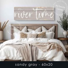 a bed with white sheets and pillows in front of a wooden sign that says river time