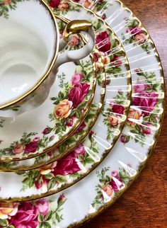 a set of four floral plates with gold trimmings and matching saucers on a wooden table