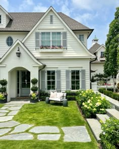 a white house with lots of green grass and flowers in the front yard, along with stone walkways