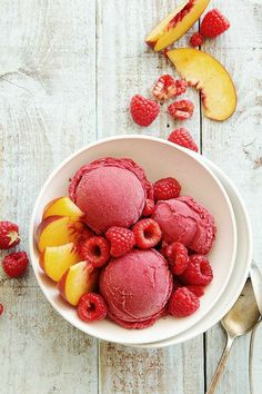 a bowl filled with ice cream and raspberries on top of a wooden table