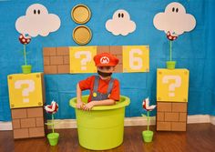 a young boy sitting in a green bucket on the floor with mario paper decorations behind him