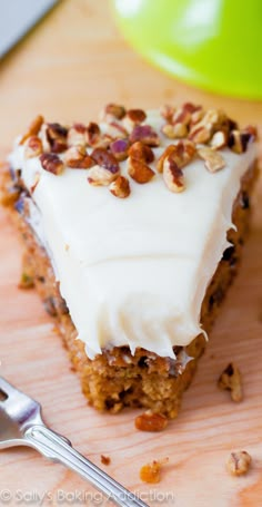 a piece of cake with white frosting and nuts on top next to a fork