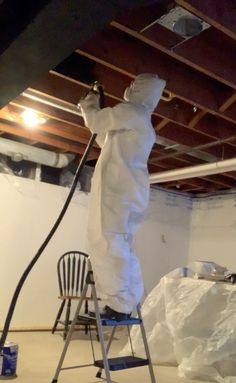 a man in white coveralls spray painting a ceiling