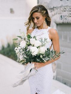 a woman holding a bouquet of white flowers in her right hand and looking at the camera