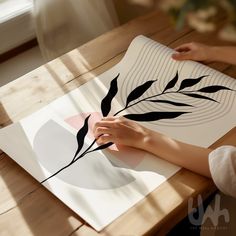 a person is drawing on a piece of paper with black and white leaves in it