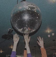 two people reaching for a disco ball in the air with their hands up to it