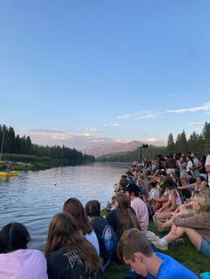 a group of people sitting on the grass next to a body of water