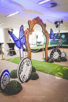 an indoor area with fake grass, clocks and butterflies on the ground in front of them