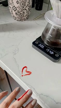 a woman's hand with red nail polish on her nails near a coffee maker