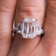 a woman's hand holding an engagement ring with three stones on the band and two sides