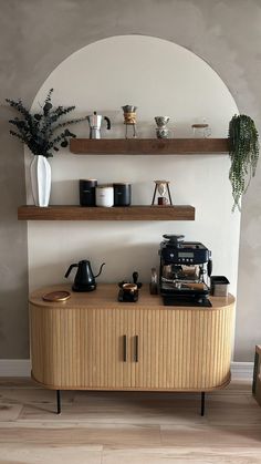 a shelf with coffee cups and other items on it in front of a potted plant