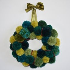 a green, yellow and blue wreath hanging on a white wall with a gold bow