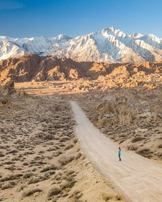 a person standing in the middle of a dirt road with mountains in the back ground