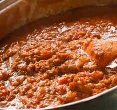 a wooden spoon in a large pot filled with chili and bread on the table next to it