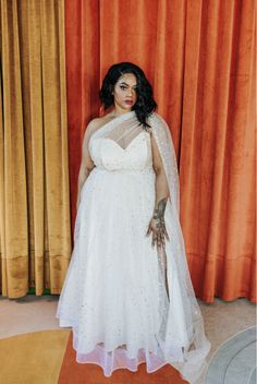 a woman in a white dress and veil posing for a photo with orange curtains behind her