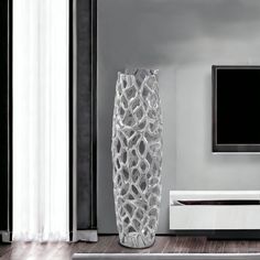 a tall white vase sitting on top of a wooden floor next to a flat screen tv