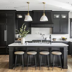 a large kitchen with black cabinets and white counter tops, two stools are in front of the island