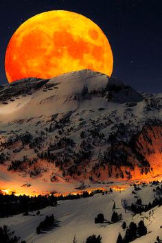 the full moon is setting over a snowy mountain