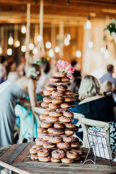 a stack of donuts sitting on top of a wooden table in front of people