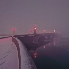 a bridge that is next to the water covered in snow and street lights at night