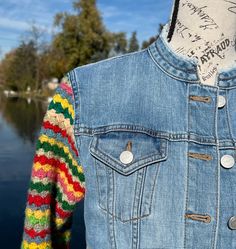 a denim jacket with multicolored sleeves hanging on a clothes line next to a body of water