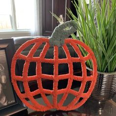 a fake pumpkin made out of yarn sitting on top of a table next to a potted plant