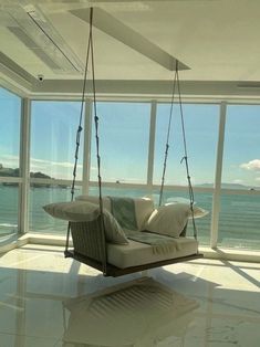 a swing chair hanging from the ceiling in front of a large window overlooking the ocean