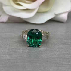 a green ring sitting on top of a table next to a white flower and a rose