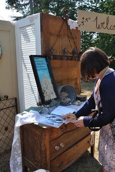 a woman standing next to an old wooden chest with writing on it and holding a pen in her hand