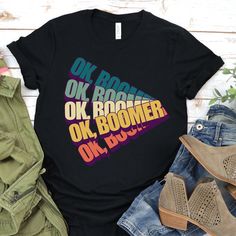 Our 'Ok Boomer Meme' shirt is viral and trendy, featuring an illustrative pop culture colloquialism 'Ok Boomer' in a retro color palette. This makes a unique present for your best friends and family for birthdays and celebrations. Gift this winner to those who love Millennial or Generation Z slang for a great laugh! Welcome to Otterly Kind Apparel! We believe in spreading kindness through our quirky designs. Each shirt comes in different sizes, colors, and styles including unisex tees, women's t Retro Black Tops With Funny Text, Retro Black Top With Funny Text, Retro Color Palette, Baby Boomer, Generation Z, Kid Tees, Perfect Shirt, Fashion Face, Trending Memes