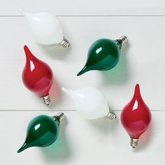 five different colored light bulbs sitting next to each other on a white wooden surface with one bulb turned green and the other red