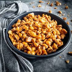 a black bowl filled with nuts on top of a gray countertop next to a towel