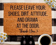 a welcome mat with a coffee cup and daisies on the table next to it that says, please leave your shoes, dirt, attitude, and drama at the door thank you