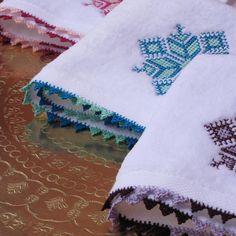 three white towels with blue and green designs on them sitting on a gold tablecloth