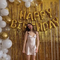 a woman standing in front of balloons and streamers with the words happy birthday on it