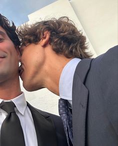 two men in suits are kissing each other while one man is wearing a white shirt and tie