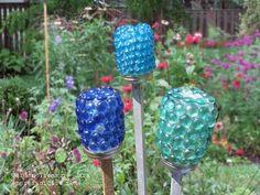 three blue and green glass vases sitting on top of metal poles in a garden