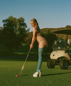 a woman in tights playing golf on the green with a white cart behind her