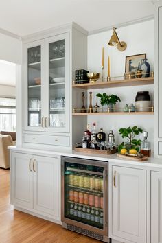 a kitchen with white cabinets and shelves filled with drinks on top of wooden flooring