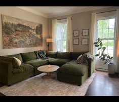 a living room filled with furniture next to two large windows and a painting on the wall